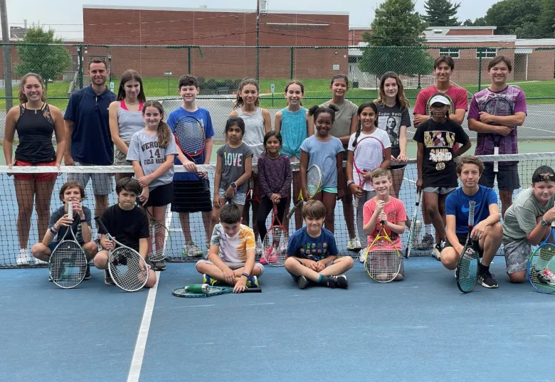 Large group of kids and coaches posing on a tennis court
