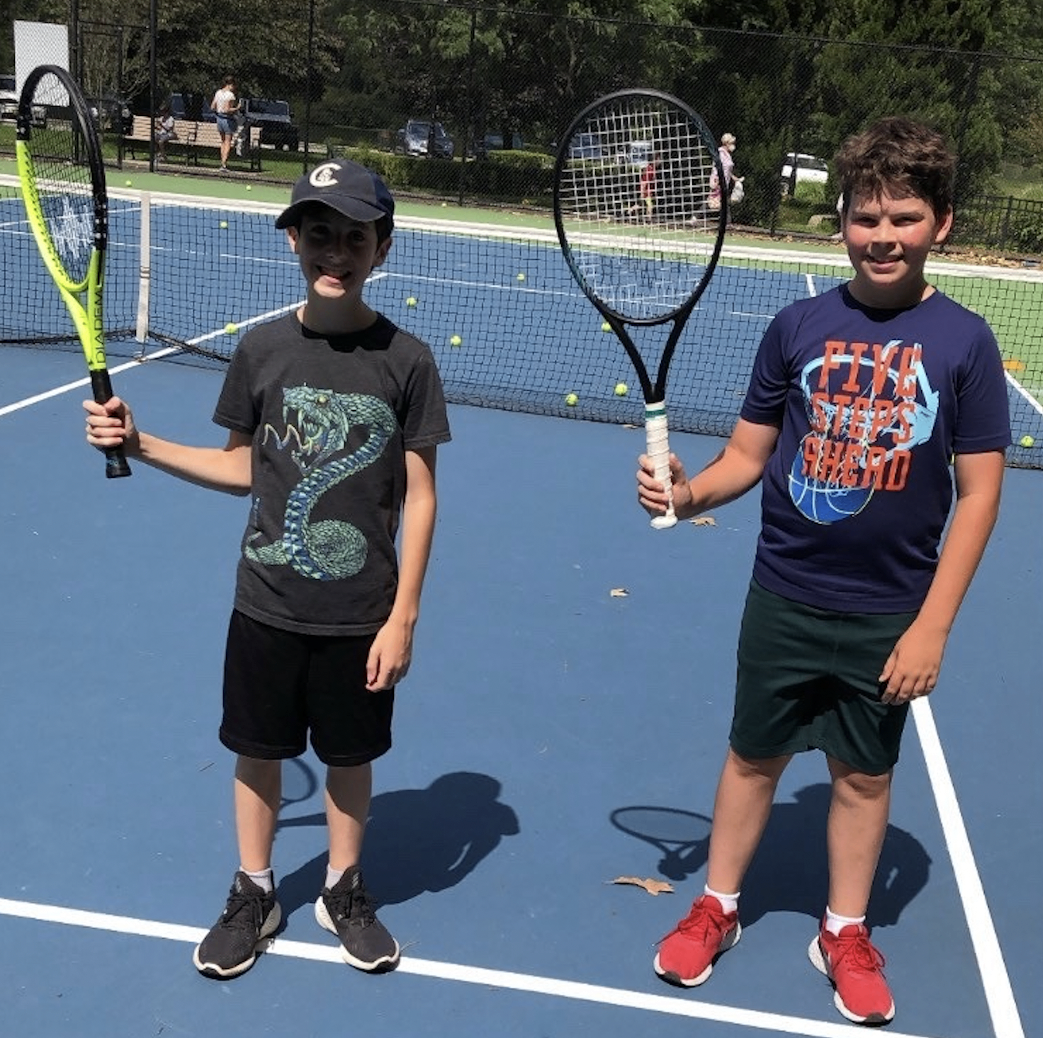 Two young students smiling and holding rackets on court